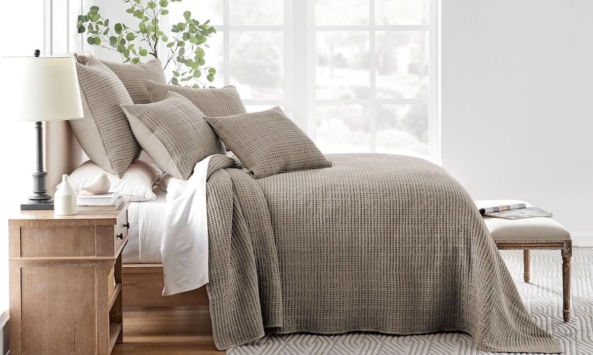 Cozy neutral bedroom with a textured cocoa color waffle quilt, matching shams, and pillows layered over crisp white bedding on a wooden bed, illustrating one of the best quilts for relaxed, modern style.