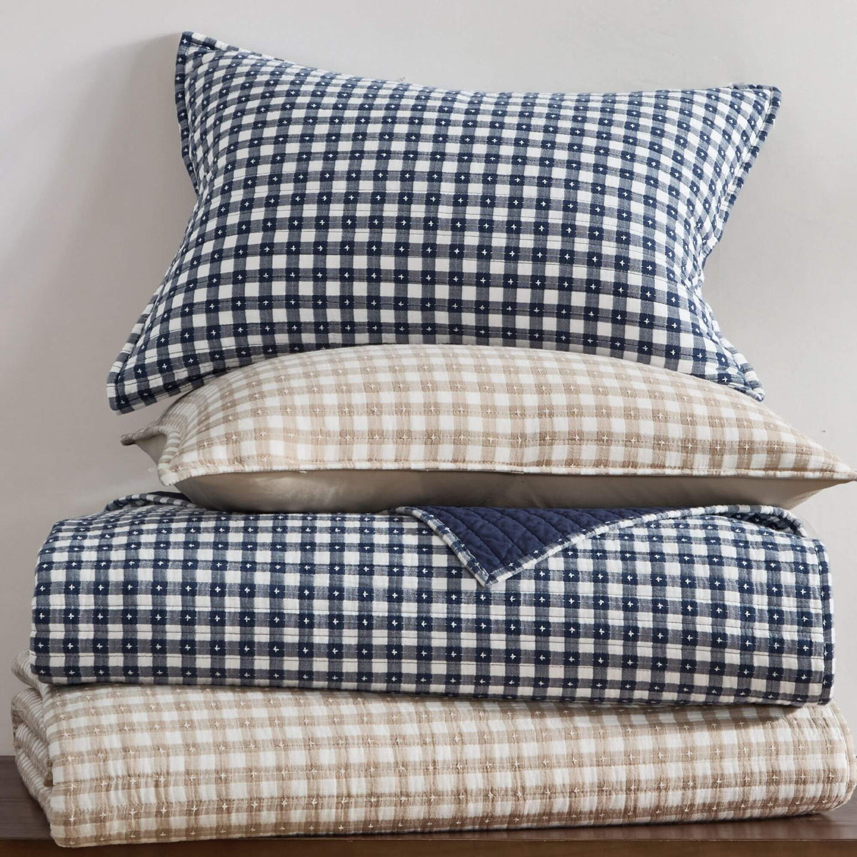 Stack of checkered bedding with blue and beige gingham patterns on a neutral background