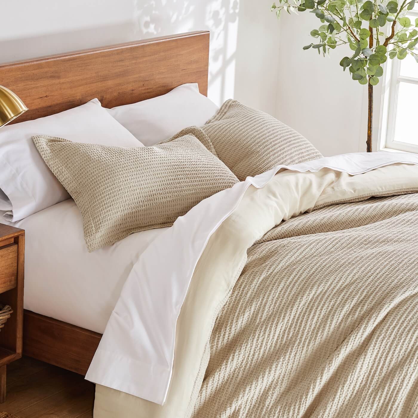 Neatly made bed with beige and white bedding in a bright bedroom.