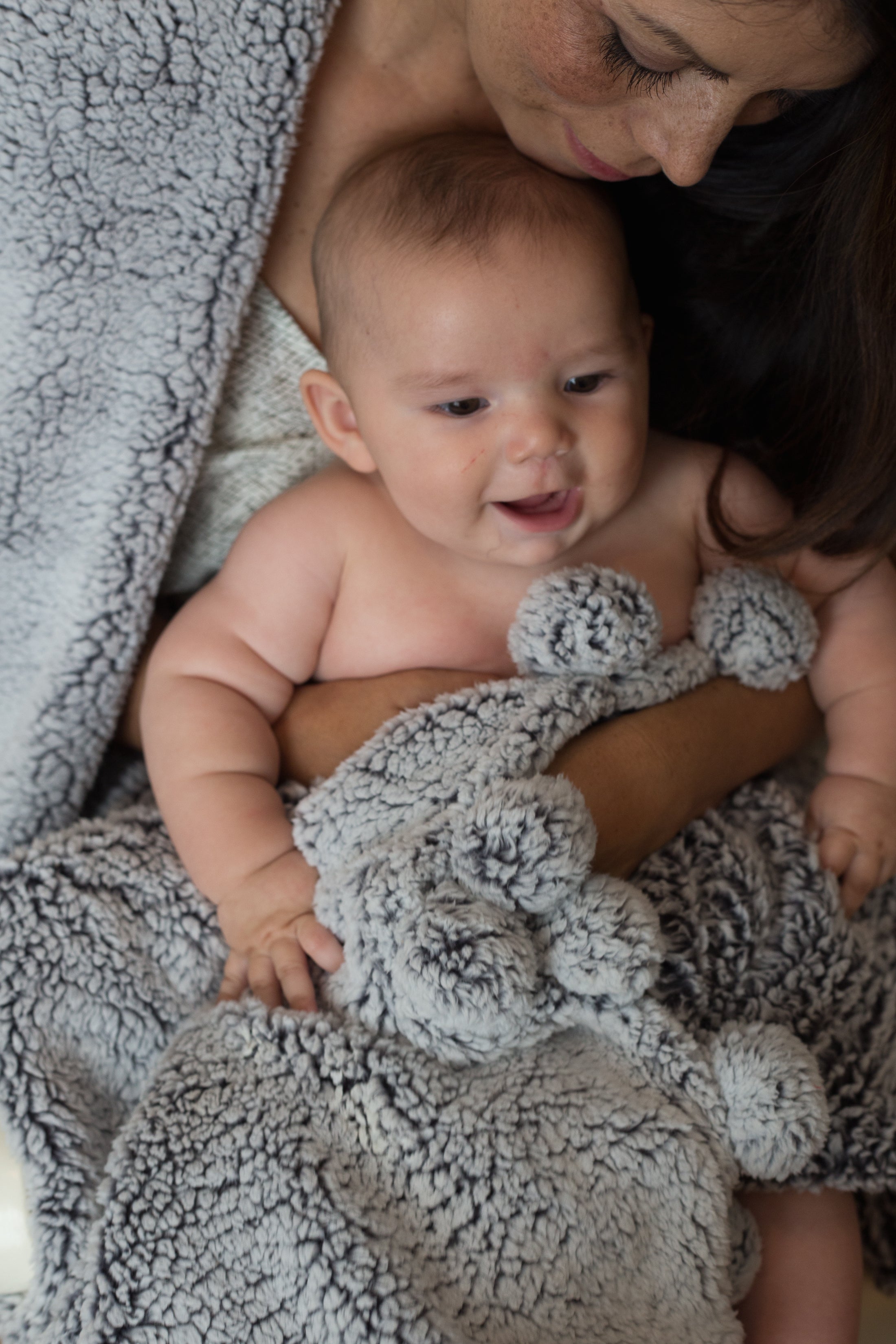 Mother holding smiling baby with gray textured blanket and stuffed animal
