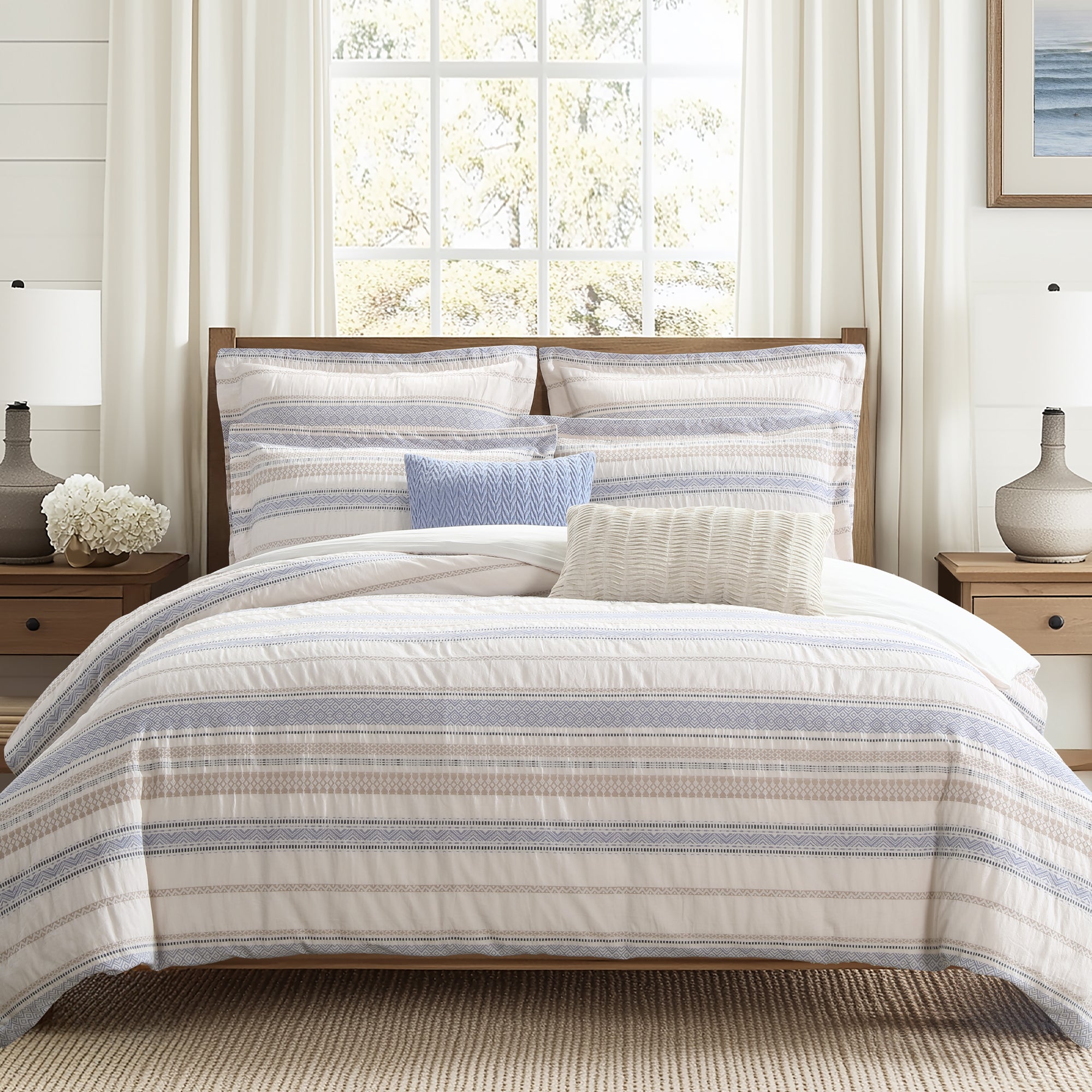 Striped bedding set on a bed in a well-lit bedroom with curtains and lamps.