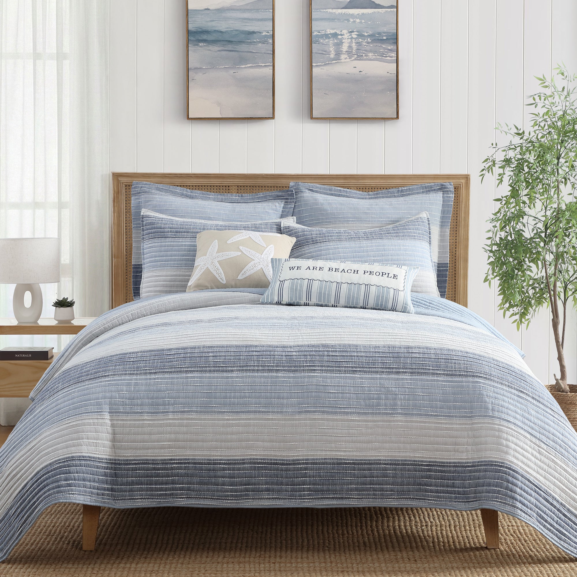Sand Stripes Blue Quilt on a bed with coastal decor, featuring softly textured horizontal striping in blue and white.