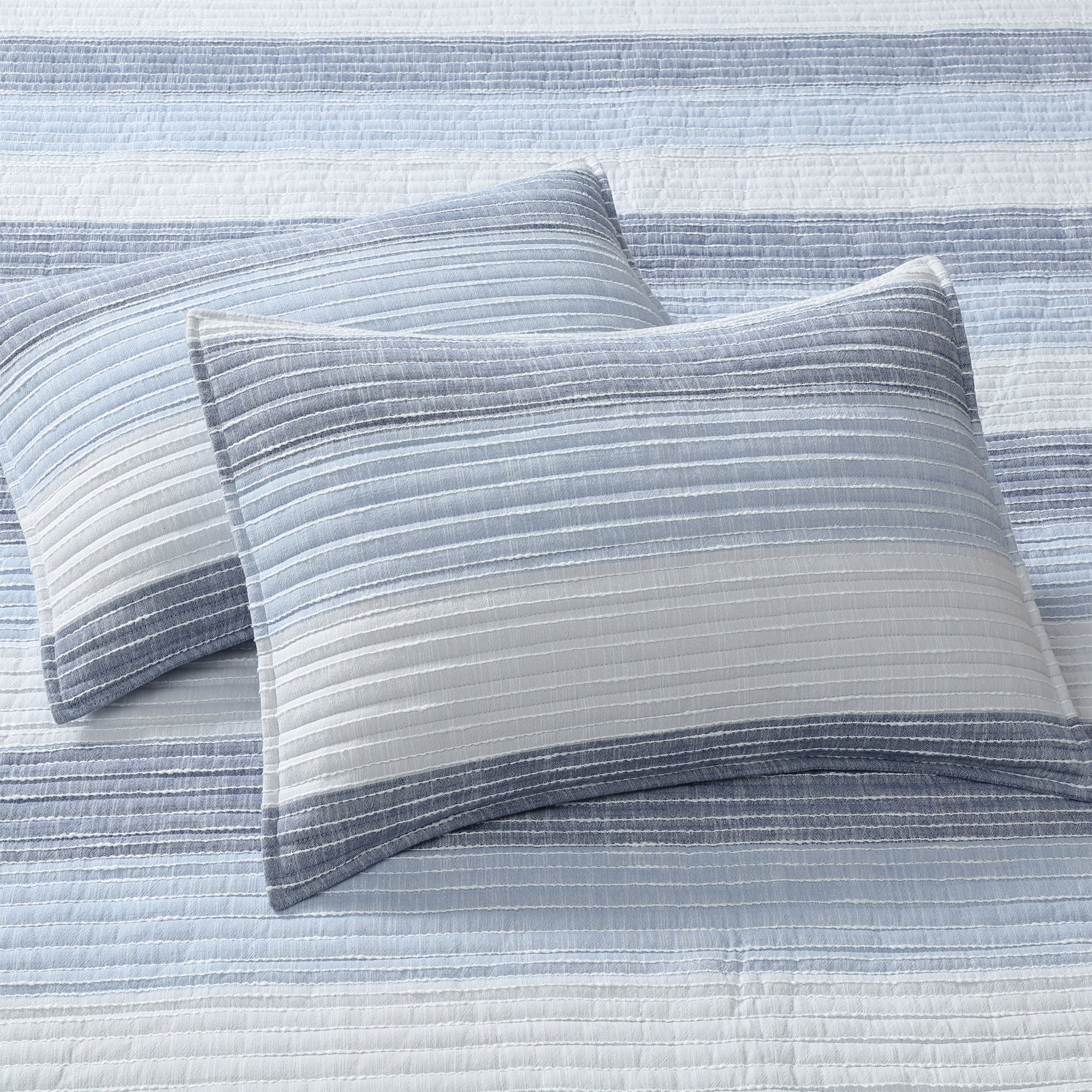 Sand Stripes Blue Quilt with two textured pillows in shades of blue and white, showcasing coastal-inspired design.