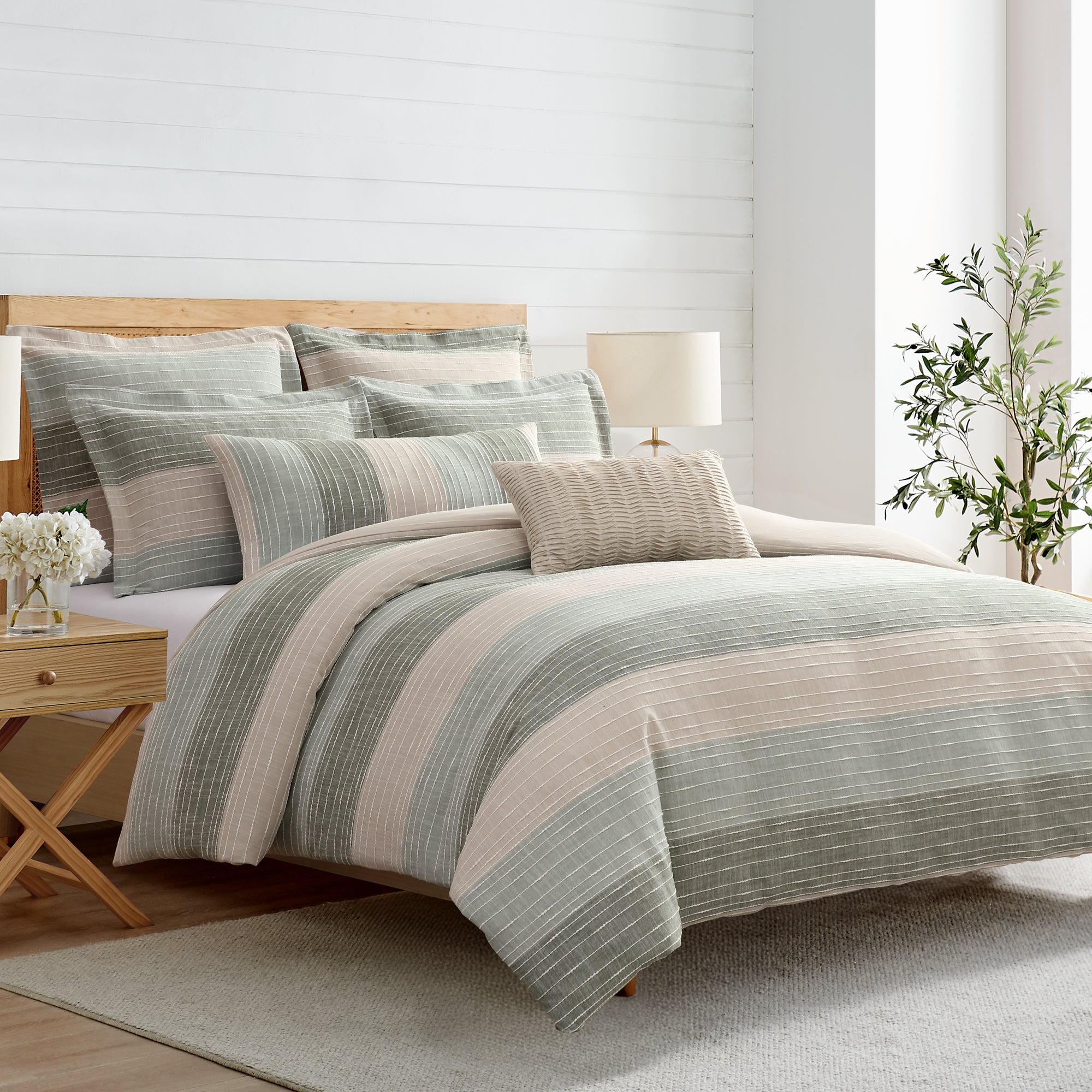 Striped bedding set on a bed in a bedroom with a lamp and plant.