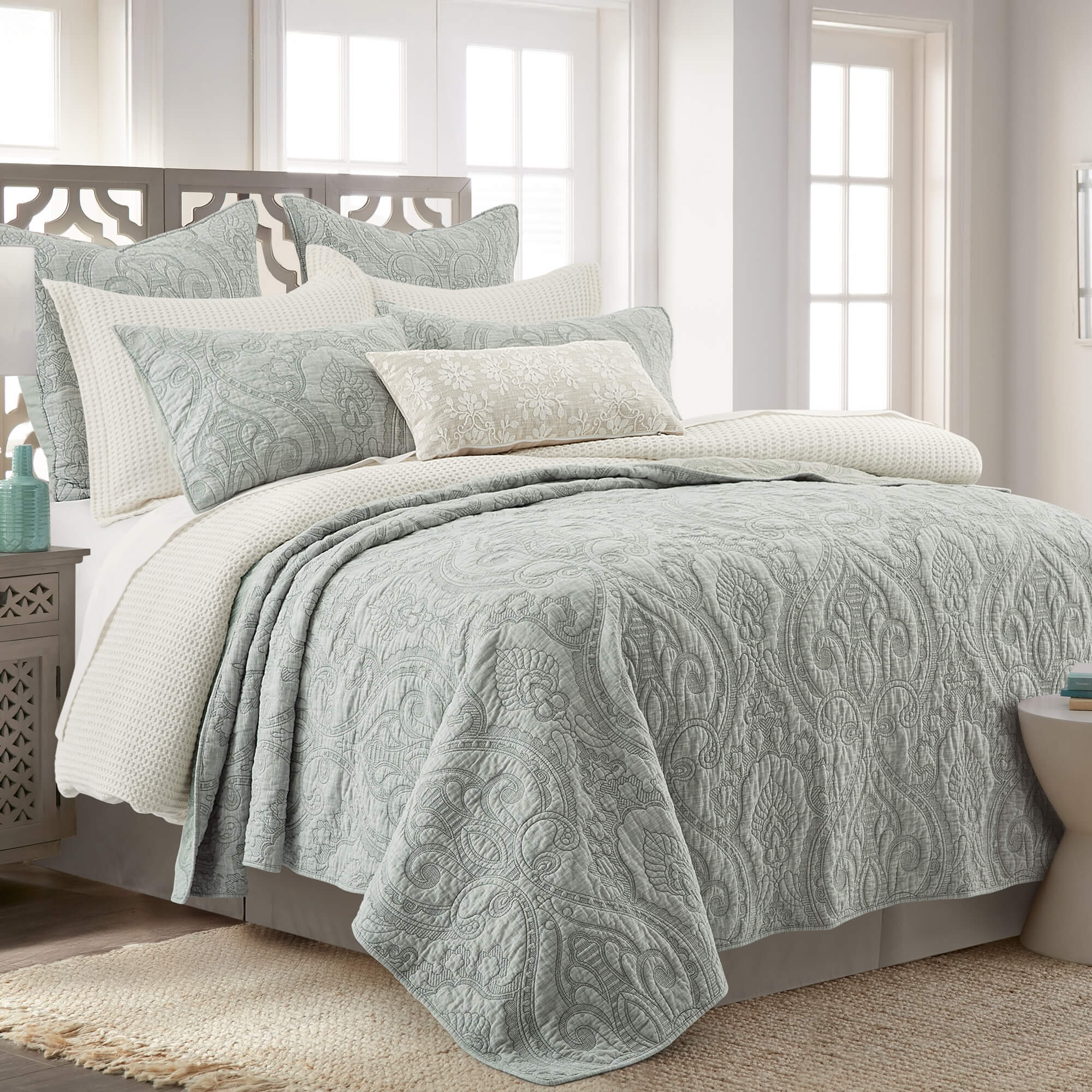 Bed with sage green patterned quilts set and pillows in a bright bedroom.