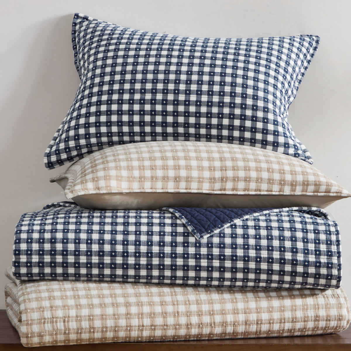 Stack of checkered bedding with blue and beige patterns on a neutral background