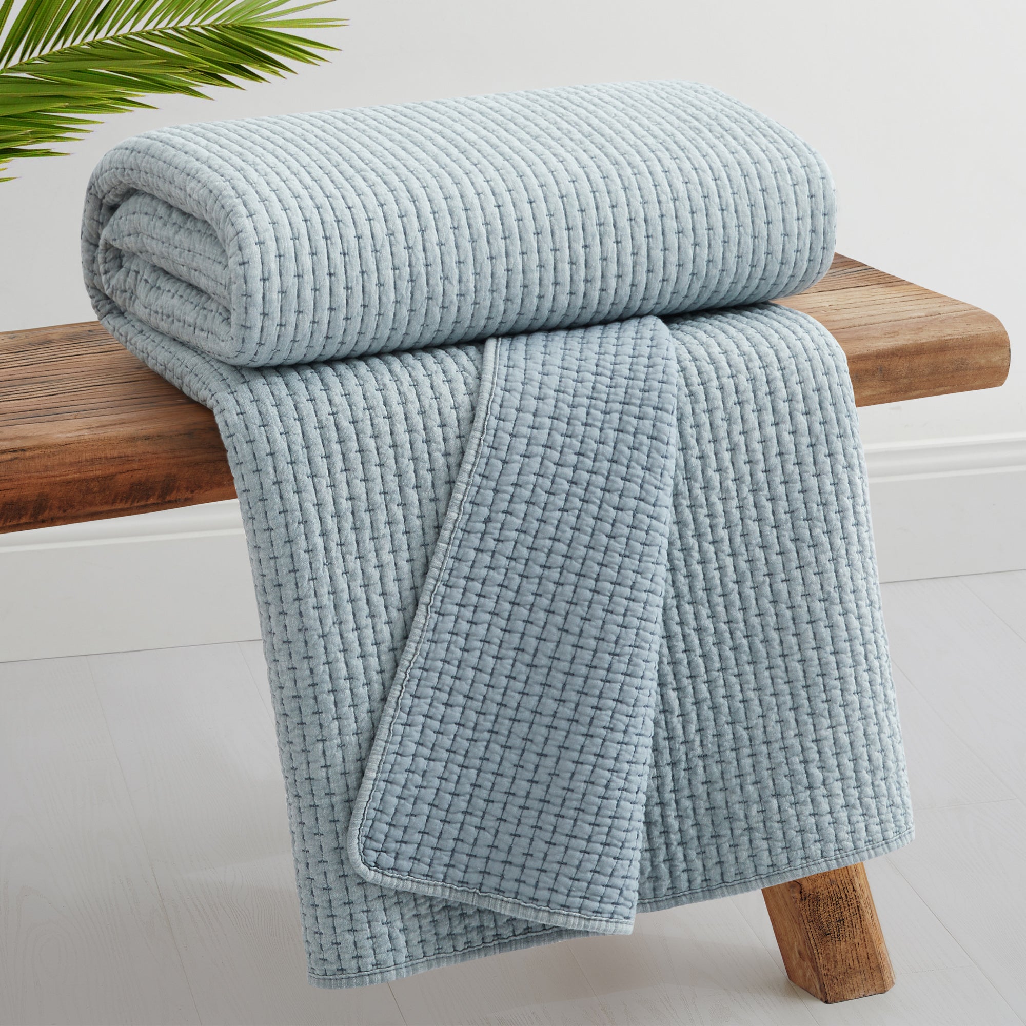 Pick-Stitch Artisan Quilted Throw rolled on a wooden table, showcasing its soft quilted texture.