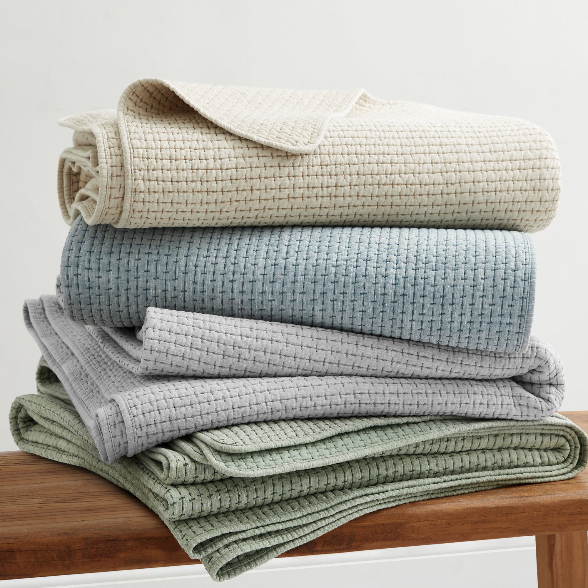 Pick-Stitch Artisan Quilted Throw stacked in neutral colors on a wooden surface, showcasing texture and comfort.