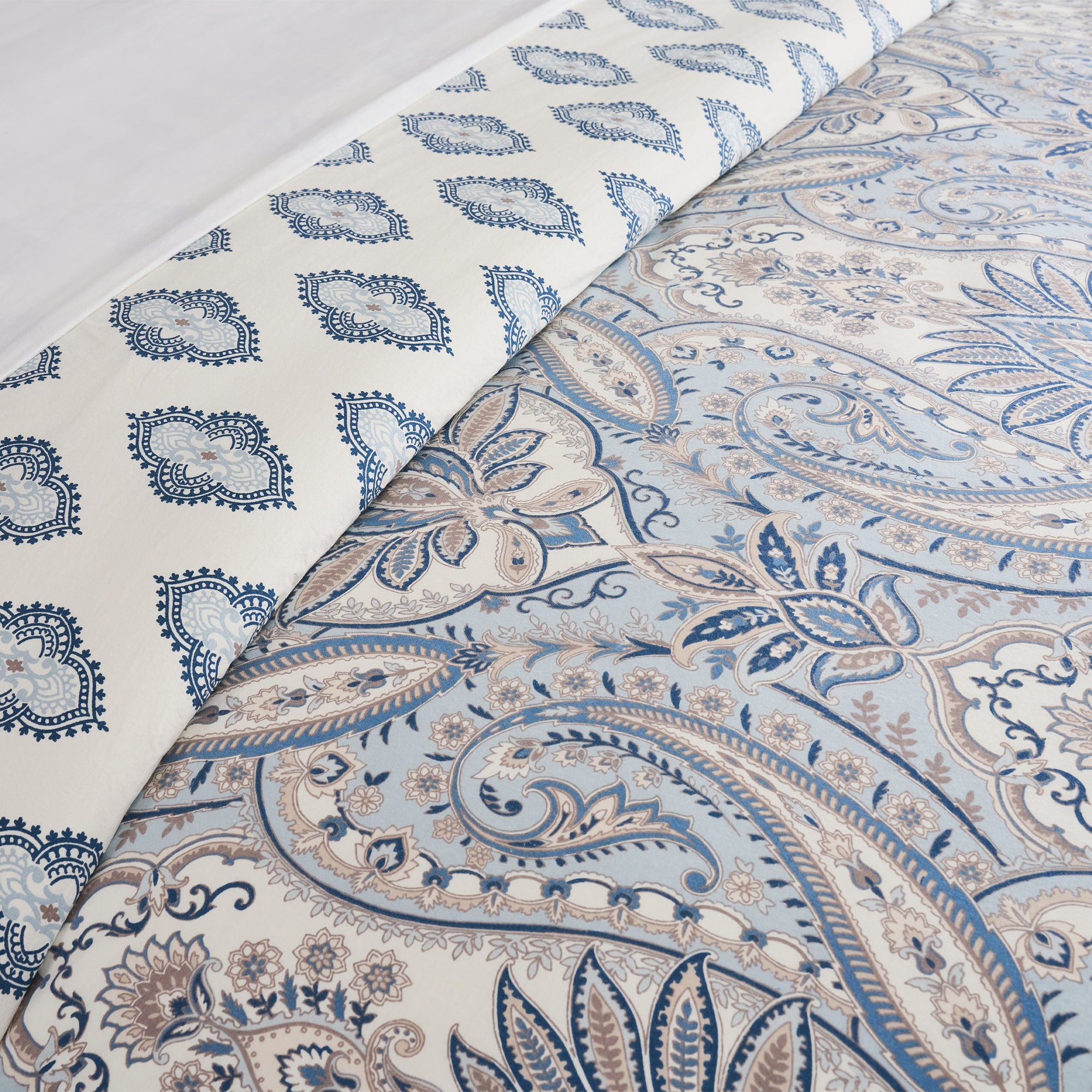 Two patterns of fabric with blue and beige paisley design on a white background