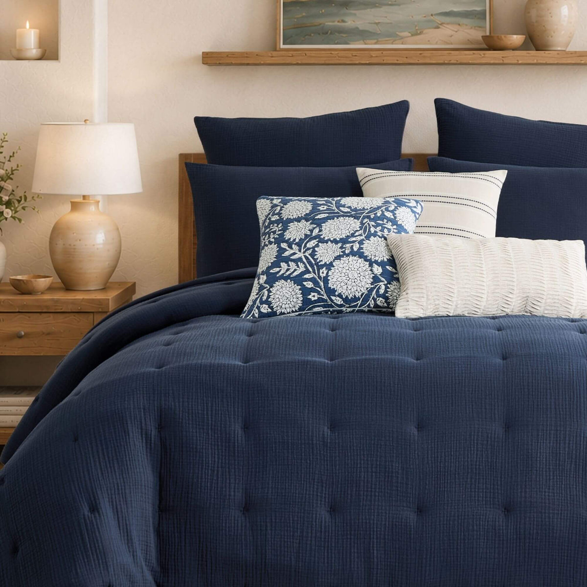 A neatly made bed in a bedroom setting, featuring a dark navy blue tufted comforter and matching pillows, with accent pillows in cream and a blue-and-white floral pattern.