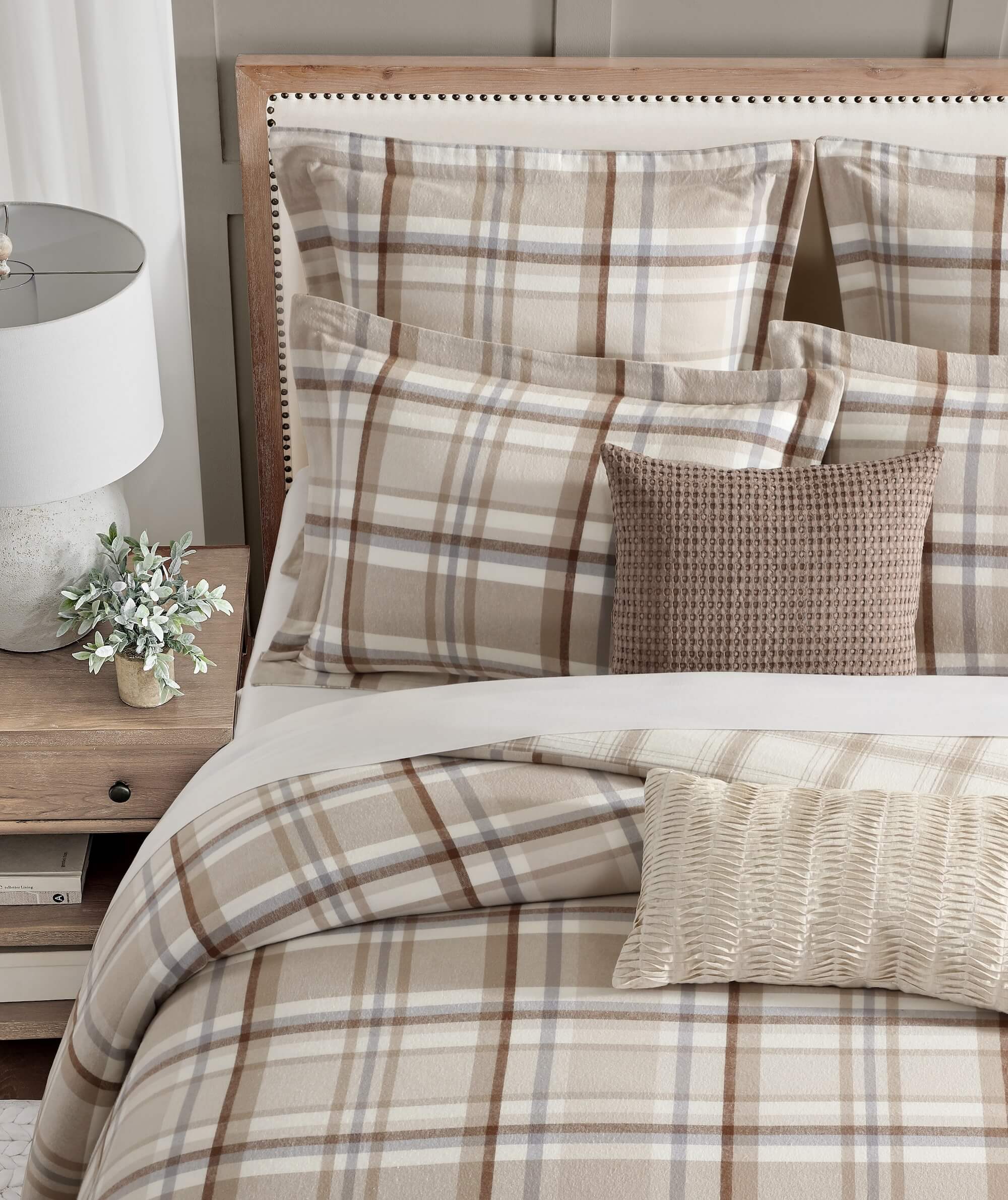 Plaid bedding set on a bed with a nightstand and lamp in a bedroom setting.