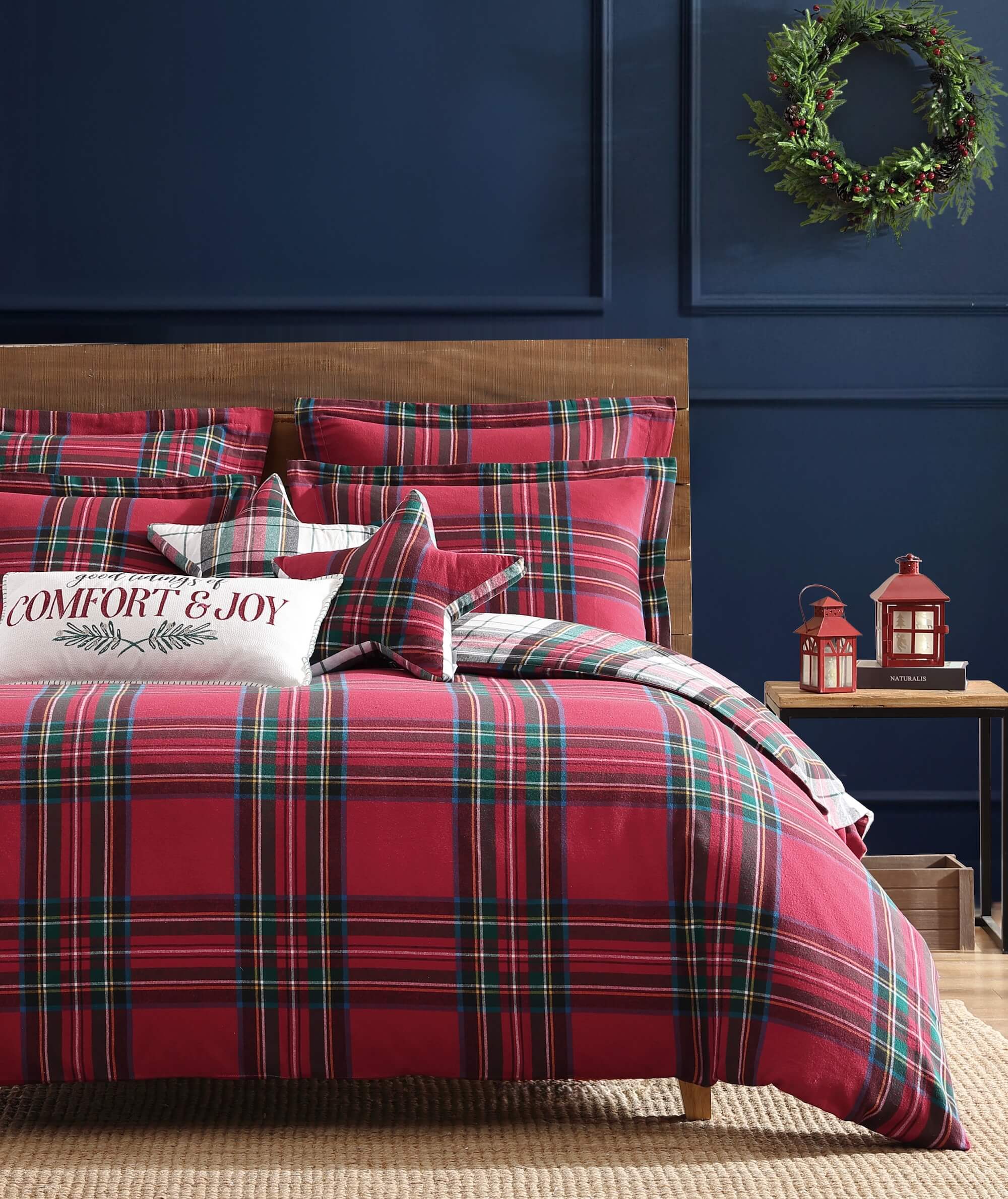 Red plaid bedding set on a bed with a decorative pillow and wreath on the wall.