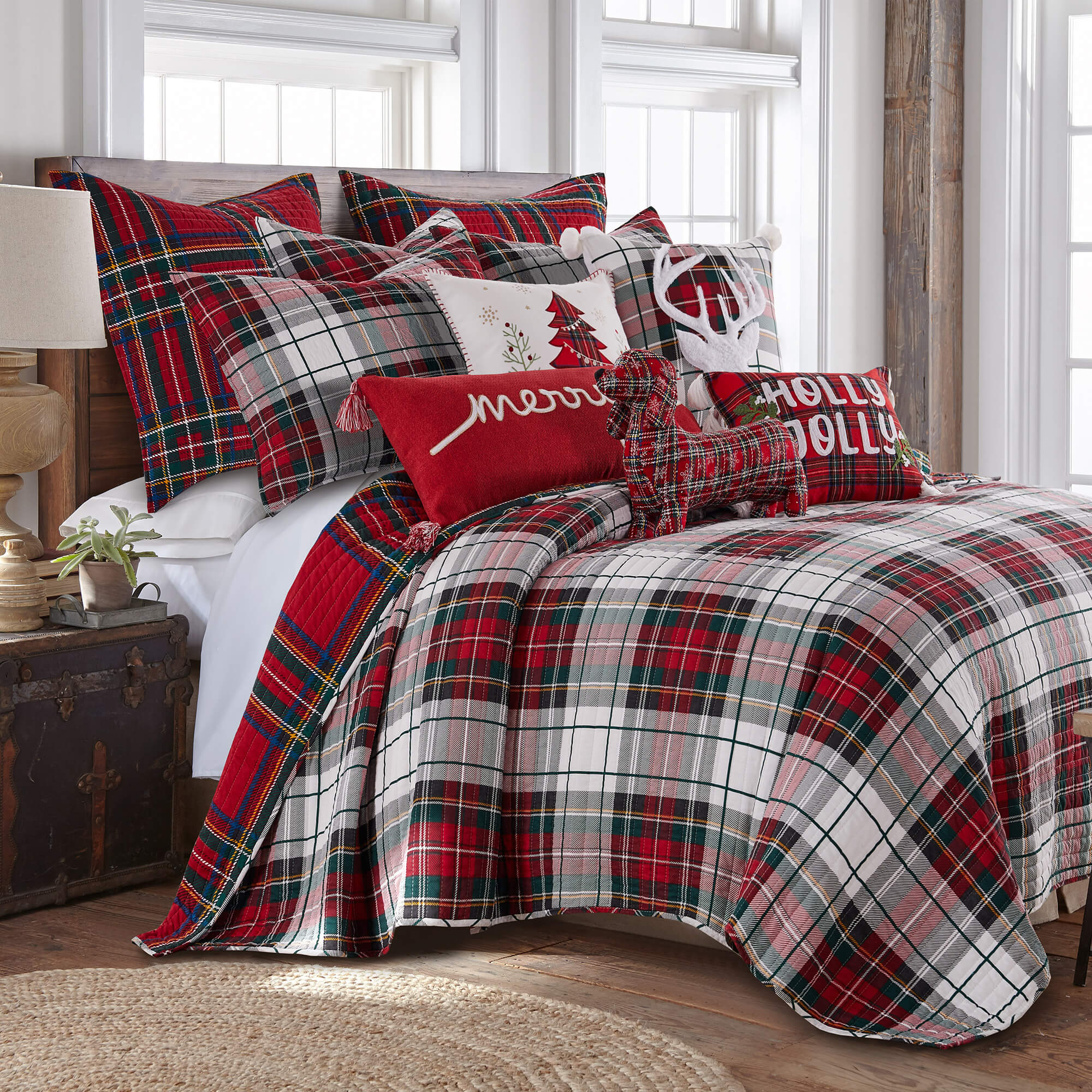 Red and white plaid Christmas quilt set with matching shams and festive holiday pillows on a cozy rustic bed in a bright farmhouse-style bedroom.