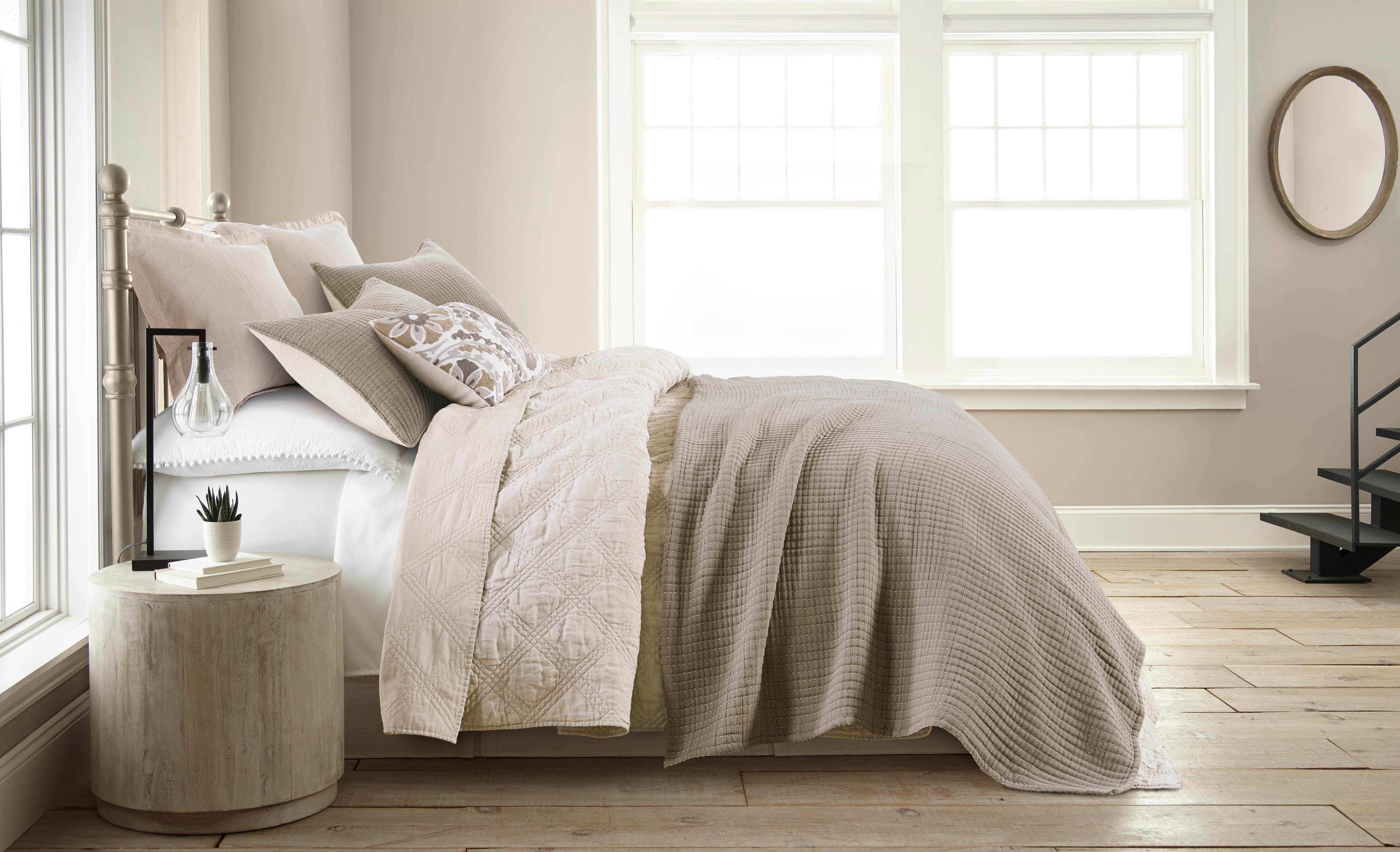 Minimalist bedroom with neutral bedding, metal bed frame, wooden nightstand, and natural light from large windows