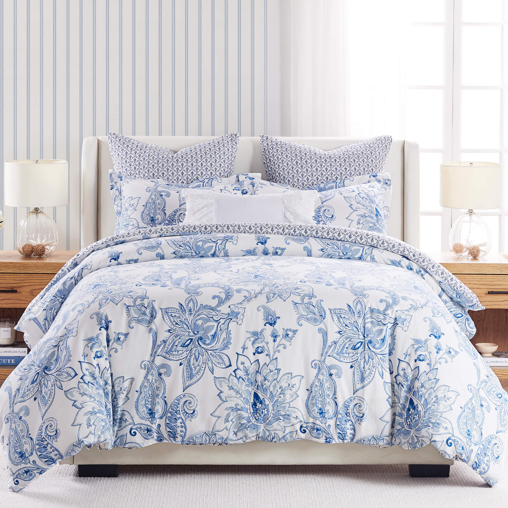 Blue and white floral king comforter set with patterned pillows on a neatly made bed in a bright, coastal-style bedroom.