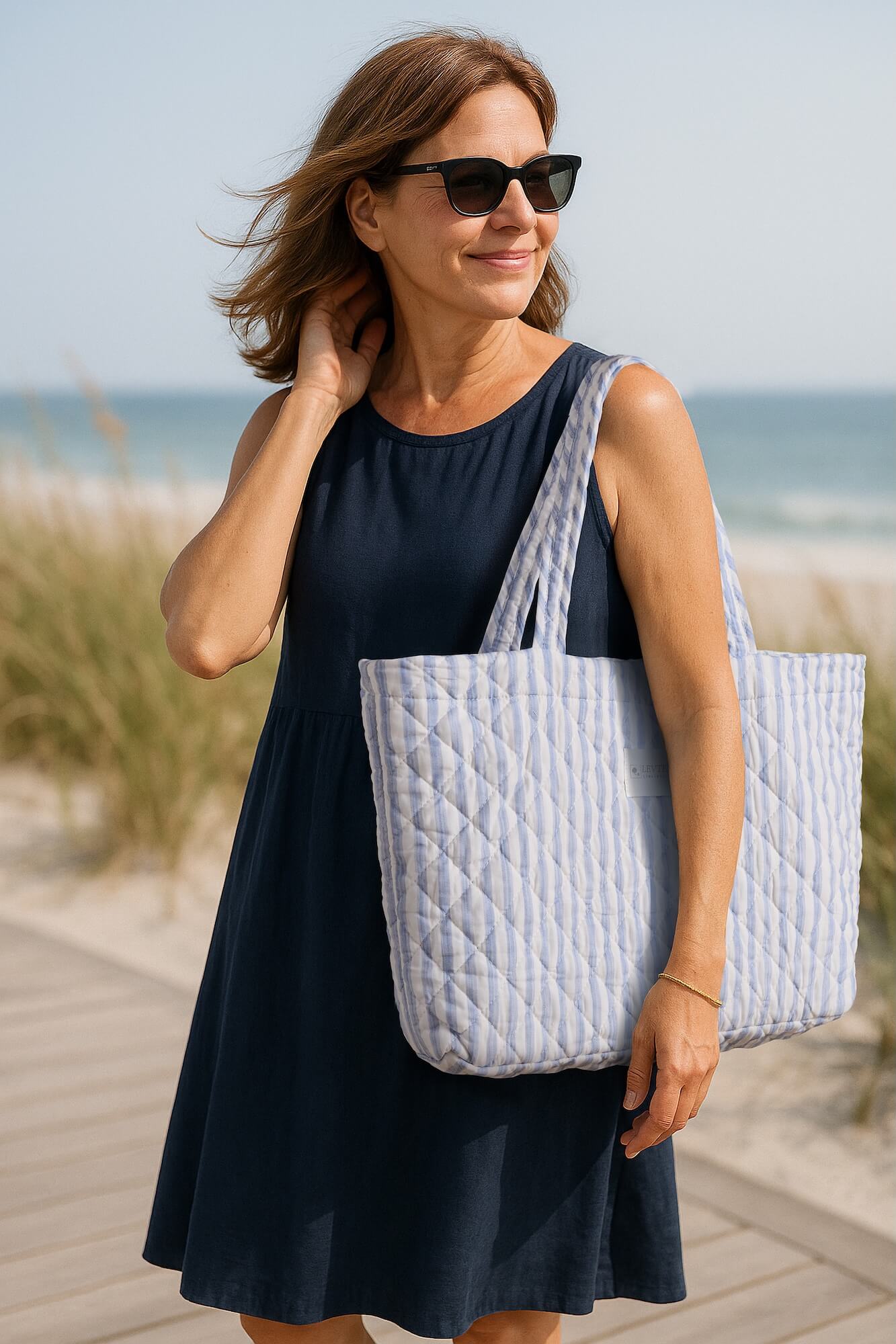 Woman at the beach in navy dress carrying Levtex Home Martha Stripe Blue tote bag featuring coastal pattern.