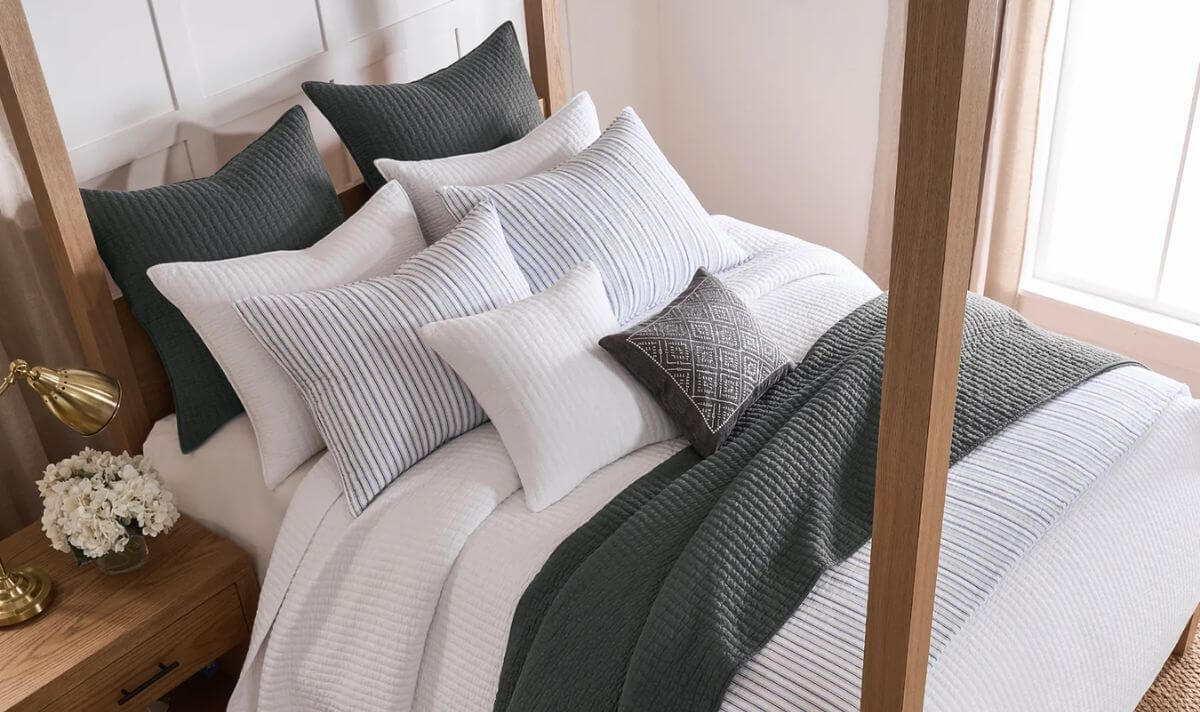 Layered bed with white quilts, gray throw, and mixed pillows on a wooden frame.