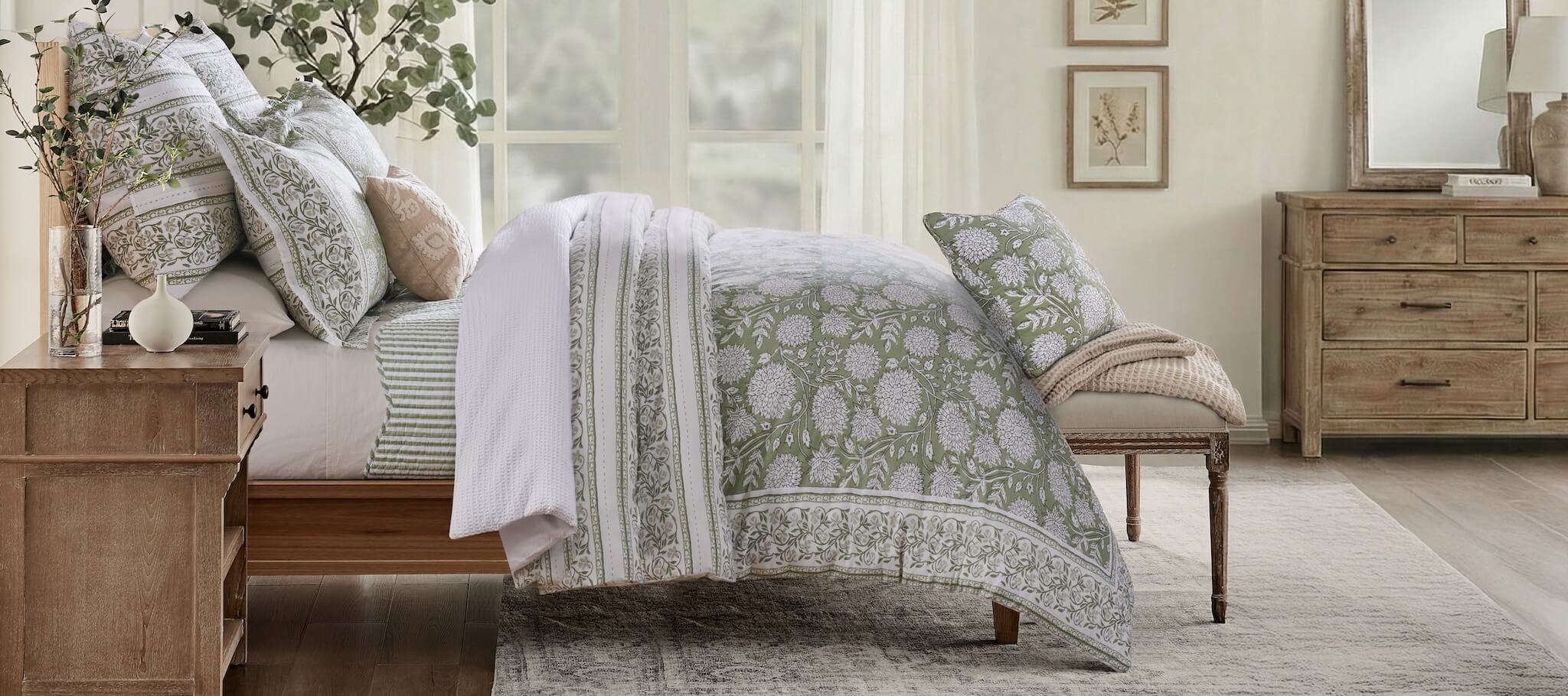 Bedroom with sage green and white floral and striped  bedding on a bed, wooden dresser, and decorative elements.