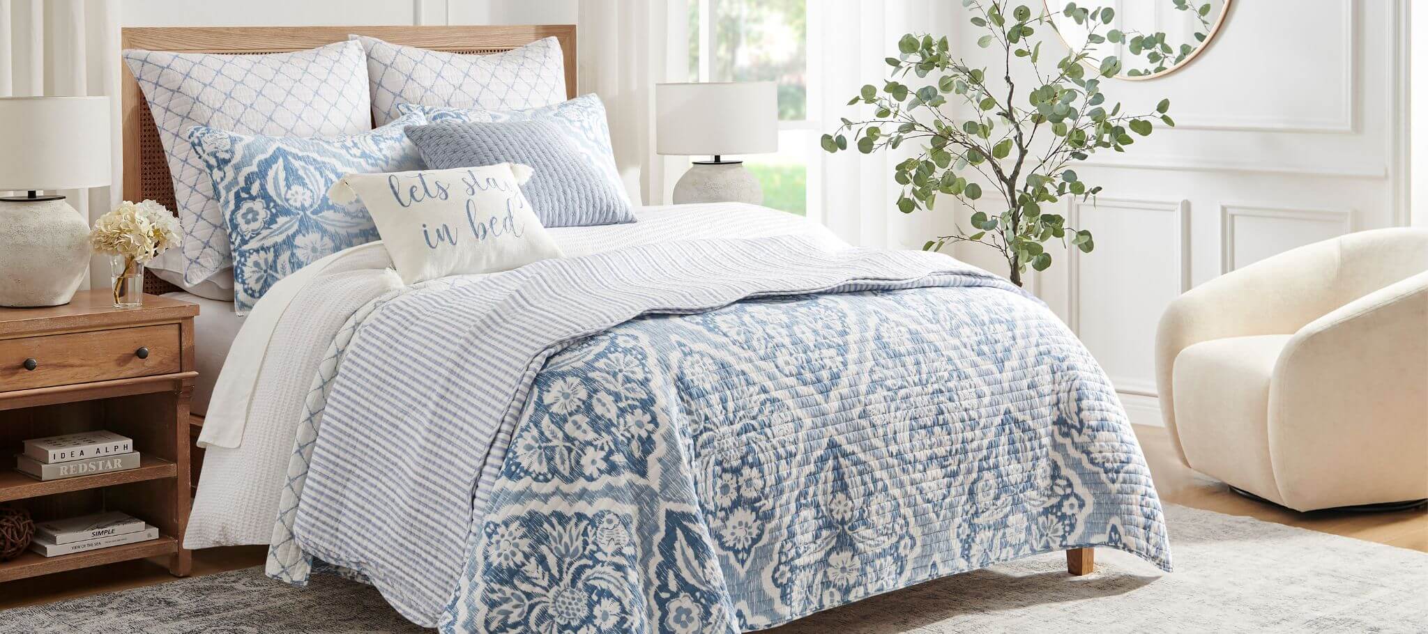 Bedroom with a bed covered in blue and white patterned bedding, pillows, and a lamp.