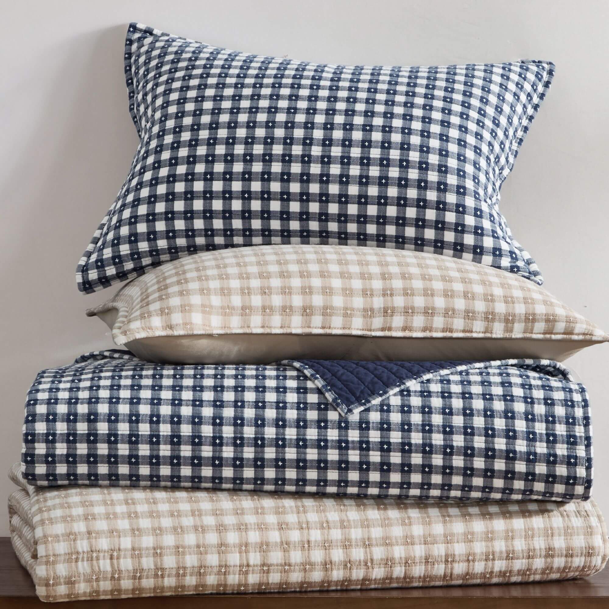 Stack of checkered bedding with blue and beige gingham patterns on a neutral background