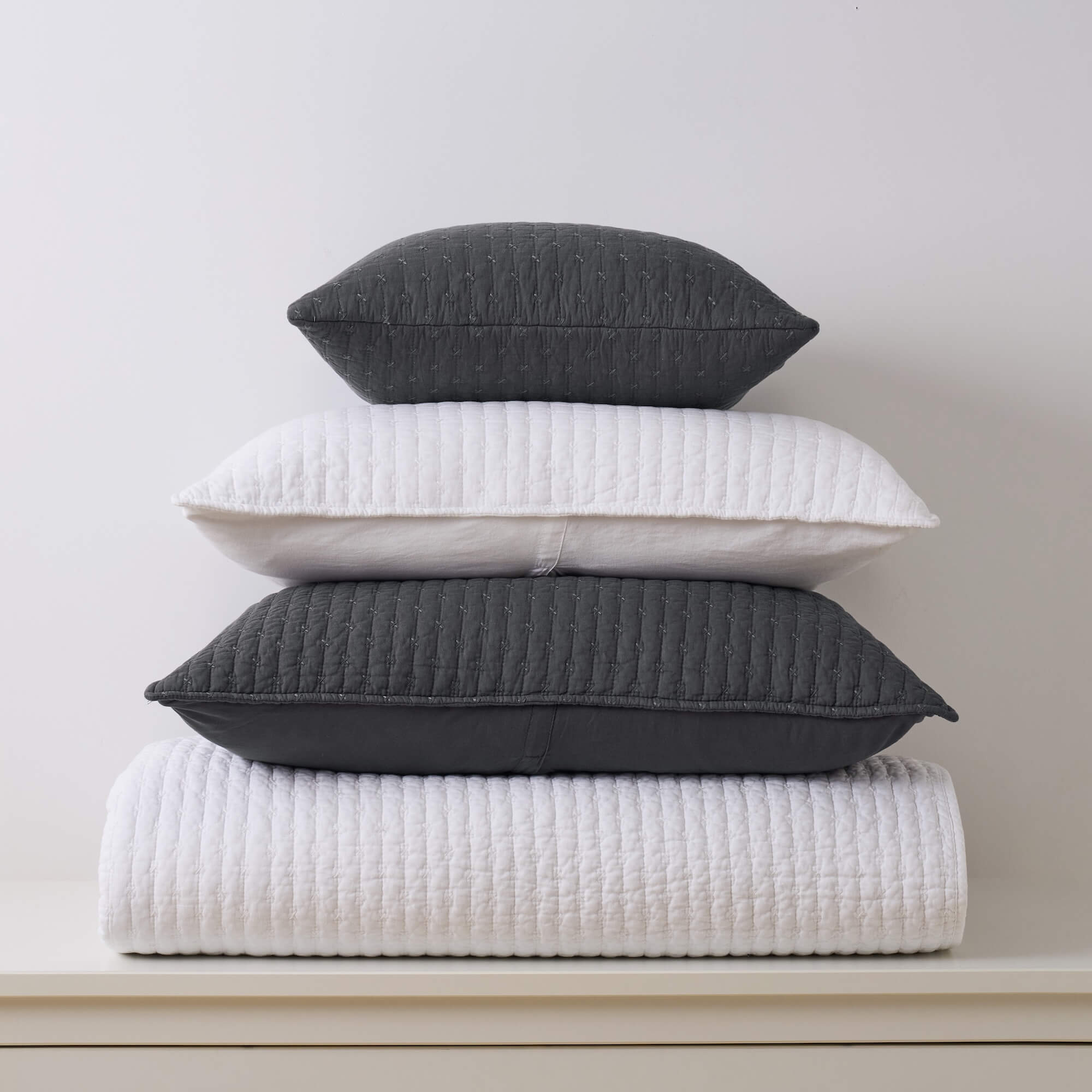 Stack of white and charcoal gray pillows on a neutral background