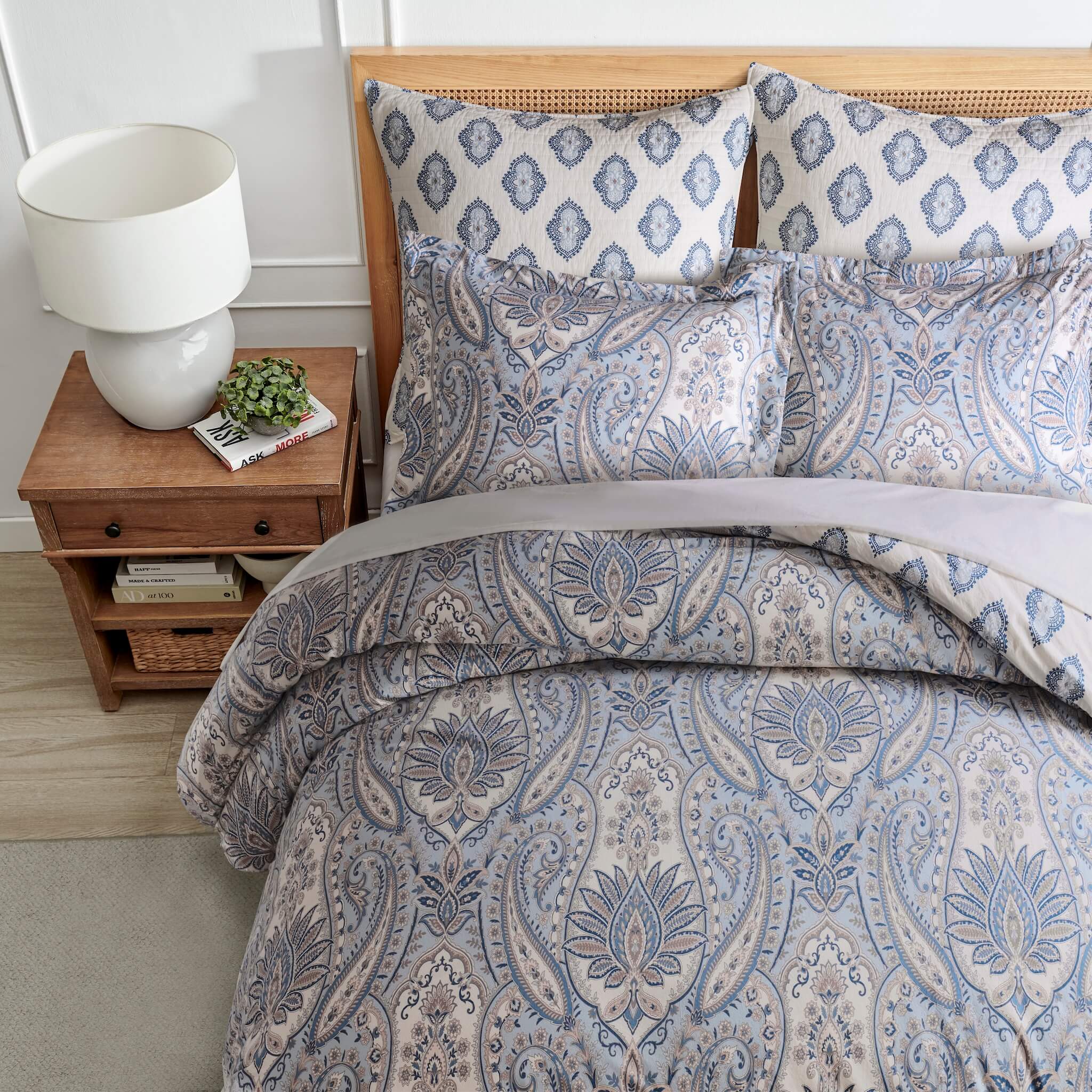 Bed with paisley patterned bedding, nightstand with lamp and plant, and wooden headboard.