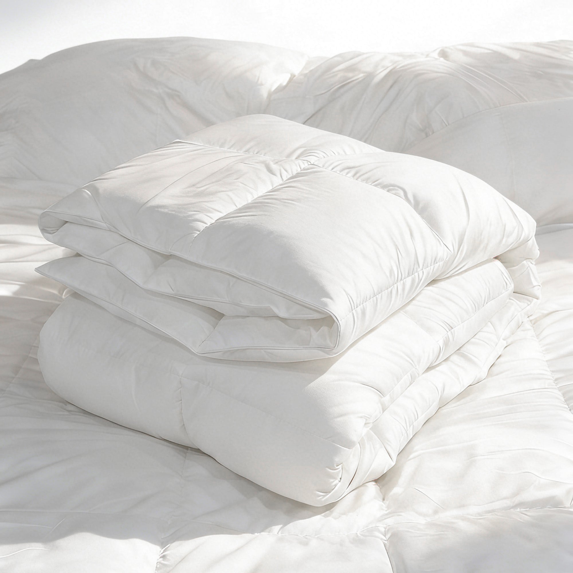 Folded white Levtex Home all-season down-alternative duvet insert with box quilting, stacked neatly on a bed to showcase its loft and smooth cotton shell.