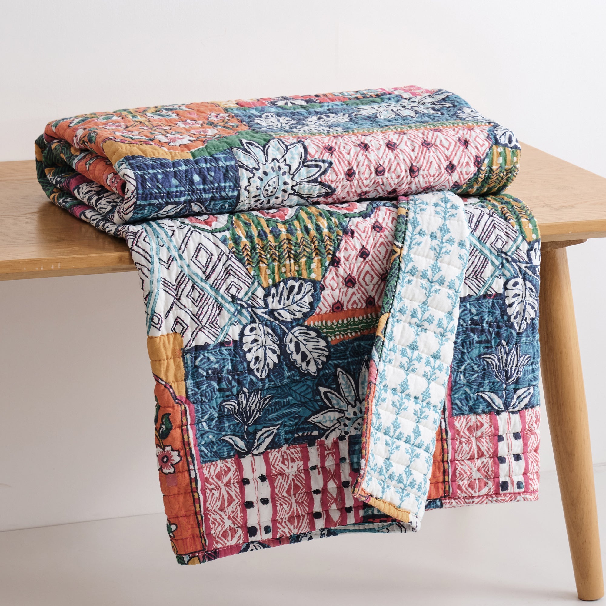 Roshita Quilted Throw displayed on a wooden table, showcasing vibrant patchwork and botanical patterns.