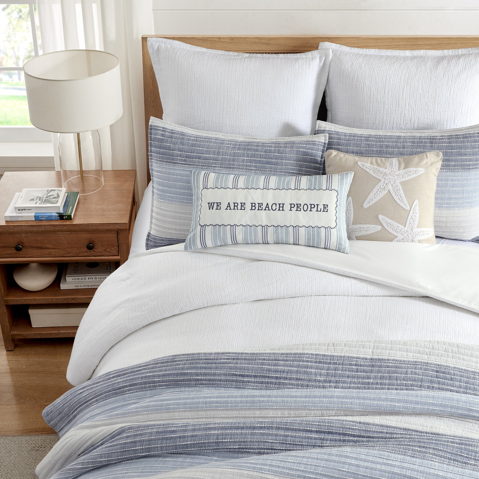 Cozy bedding featuring the Sand Stripes Blue Quilt with pillows and a beach-themed accent in a coastal-inspired bedroom.