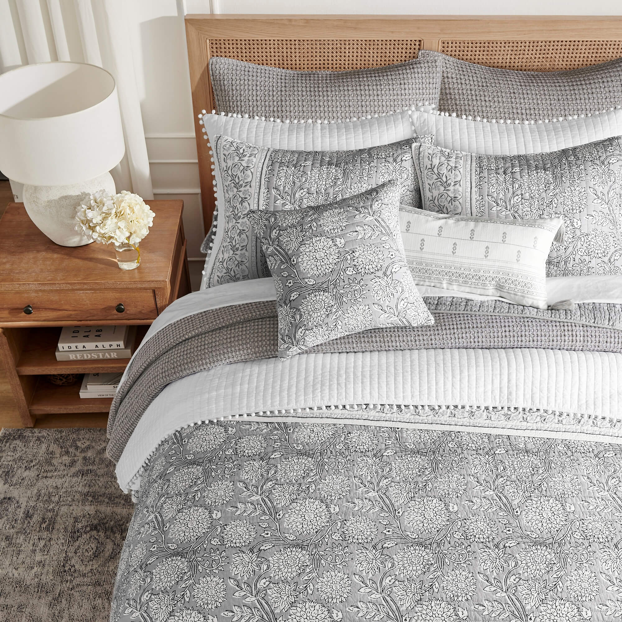 Gray and white floral pattern quilt set on a bed with a wooden headboard and nightstand.