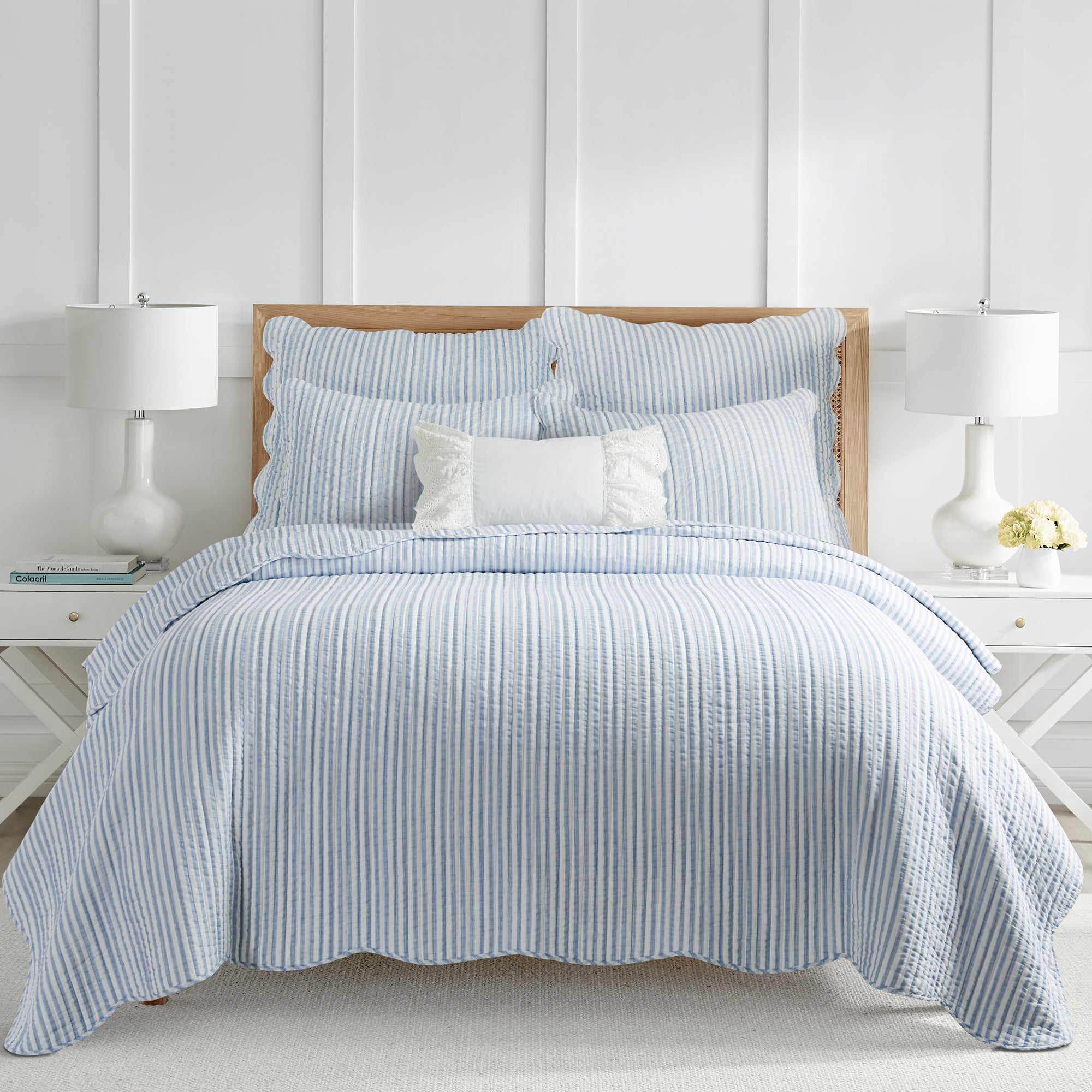 Cozy bedroom featuring a neatly made bed with light blue and white vertical striped coastal quilt set with scalloped edges and matching shams 