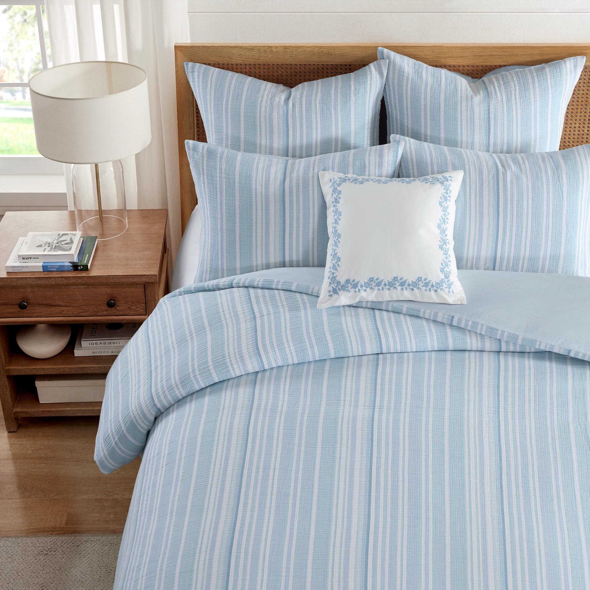 Boracay Stripe Floral Embroidered Pillow on a bed with blue striped bedding and decorative pillows