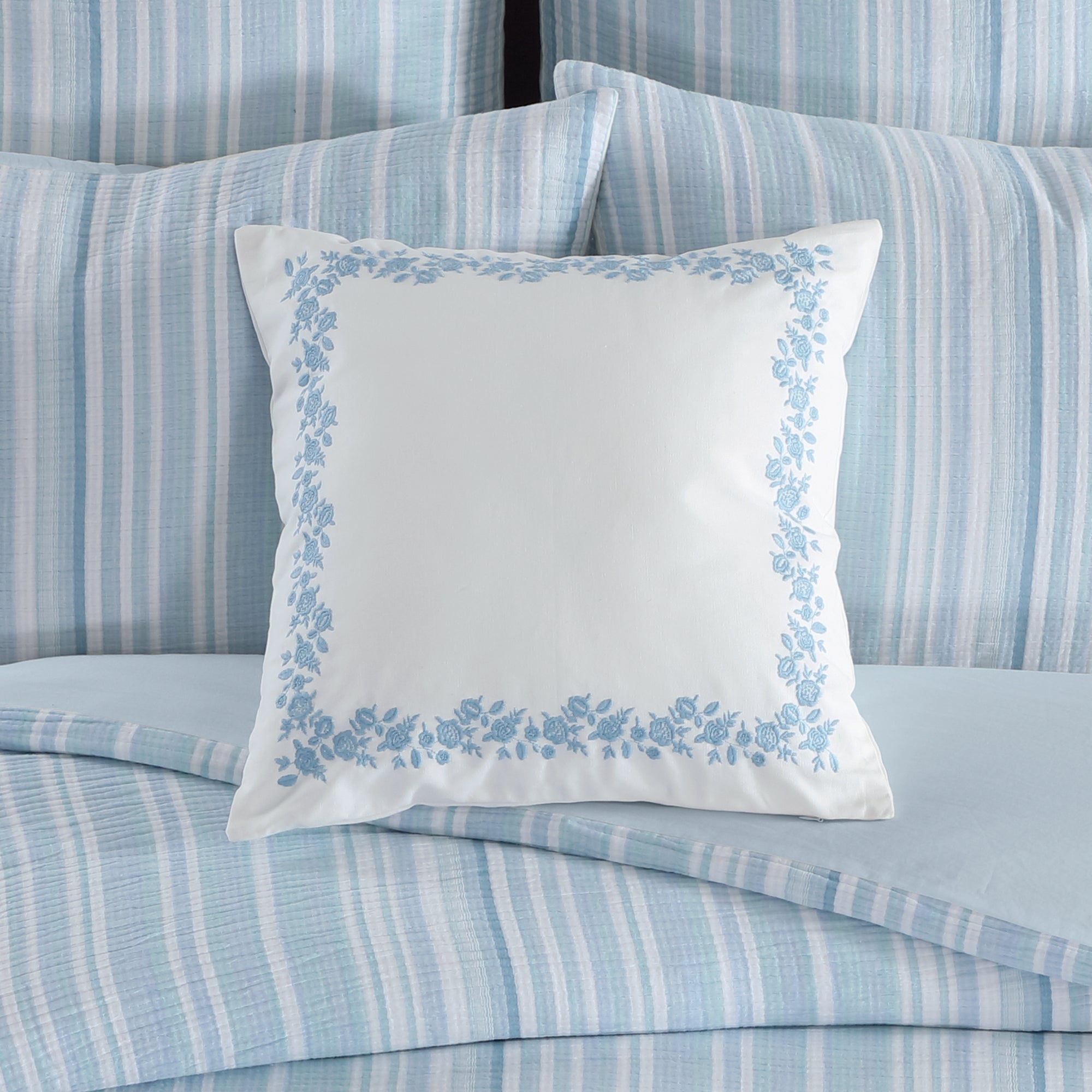 Boracay Stripe Floral Embroidered Pillow on a bed with blue striped bedding.