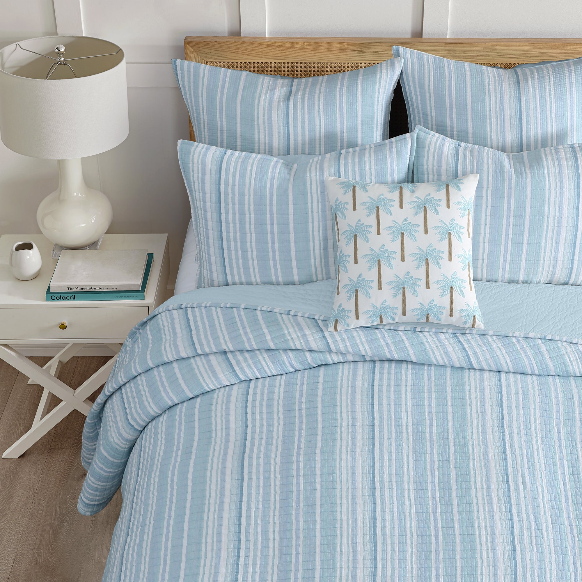 Boracay Stripe Crewel Palm Tree Pillow featured on a blue-striped bedspread in a cozy bedroom setting.