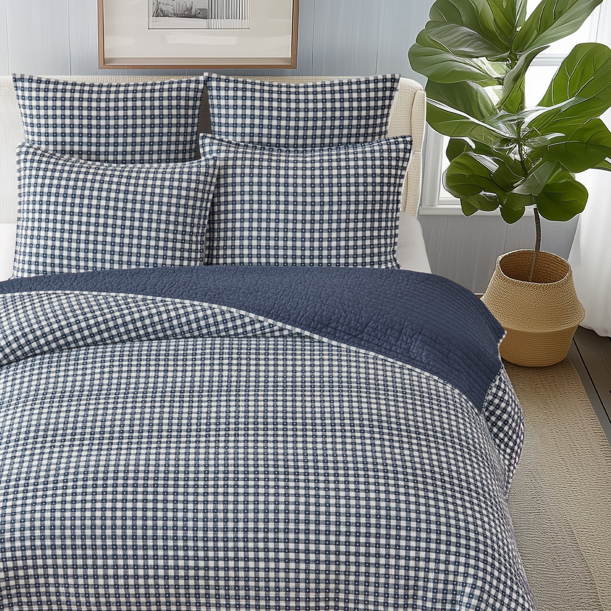 Bed with blue and white checkered bedding in a room with a plant and framed picture.