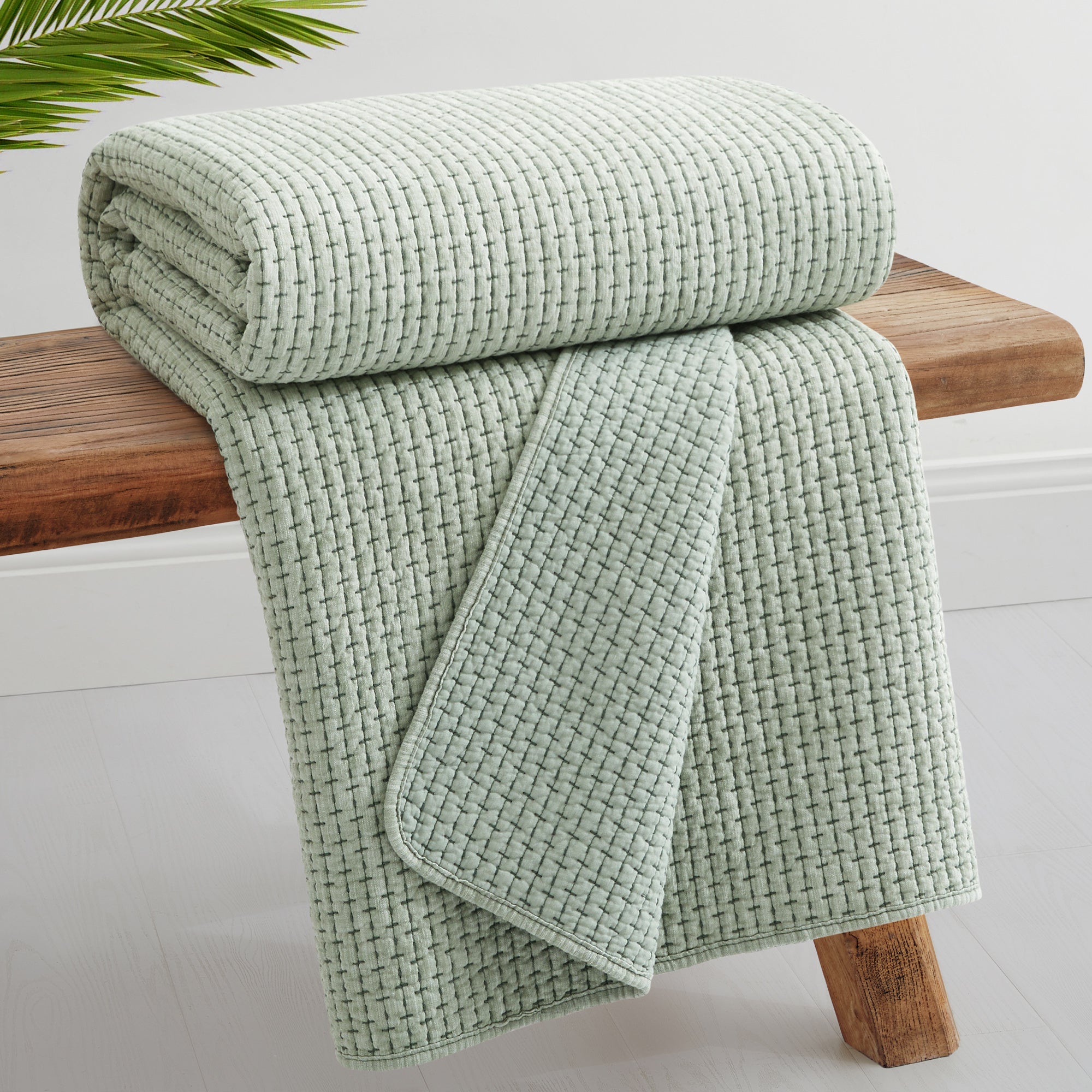 Pick-Stitch Artisan Quilted Throw in soft green color, showcasing a textured quilted surface on a wooden bench.