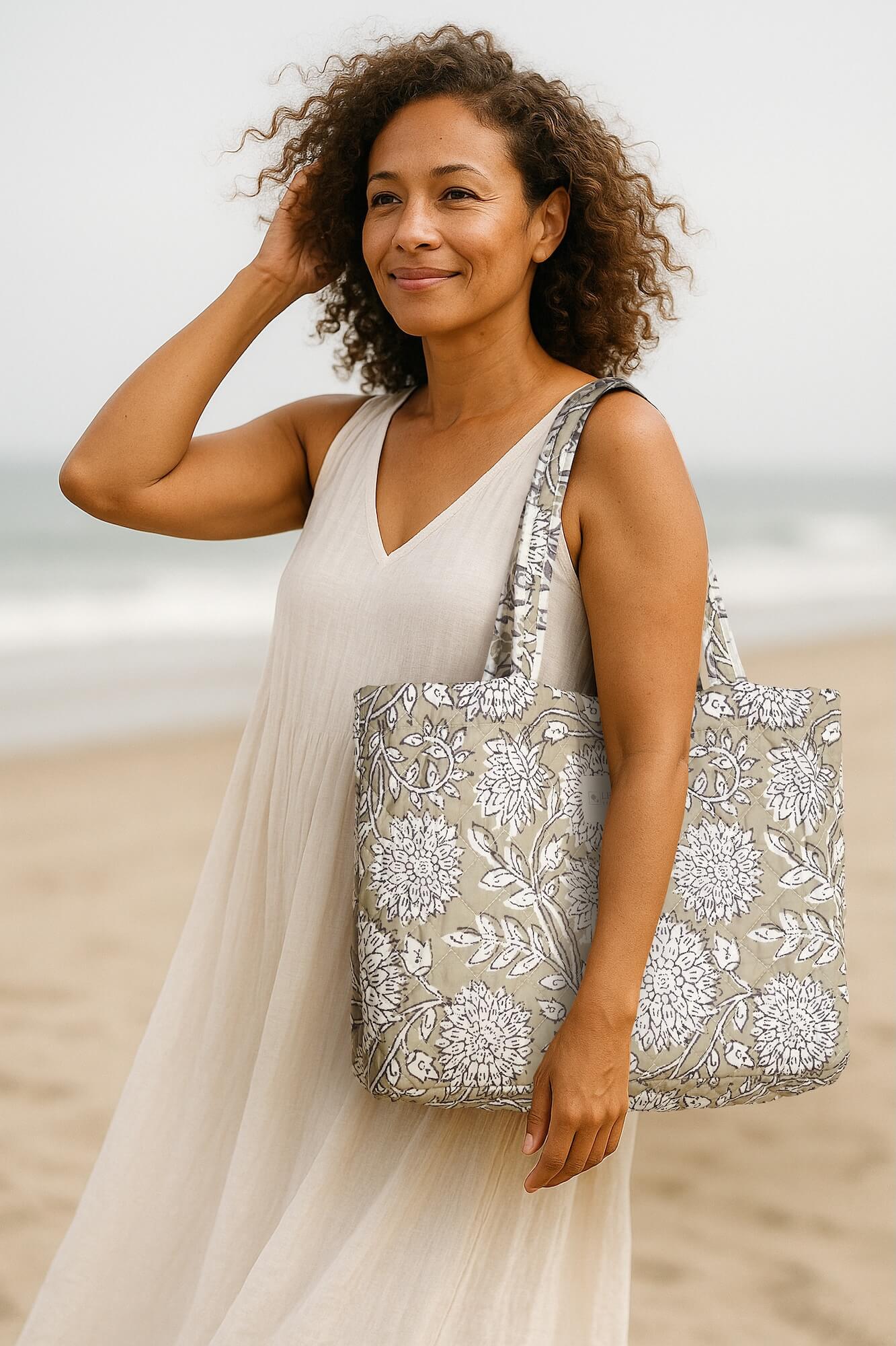 Woman at the beach in navy dress carrying Levtex Home Adare Taupe tote bag featuring floral pattern.